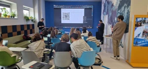 Młodzież rozwiązuje cyfrowe zagadki na urządzeniach elektronicznych, w tle jest duży ekran – 