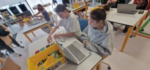 Uczniowie siedzą w ławkach i uczą się programowania z użyciem klocków LEGO SPIKE – 